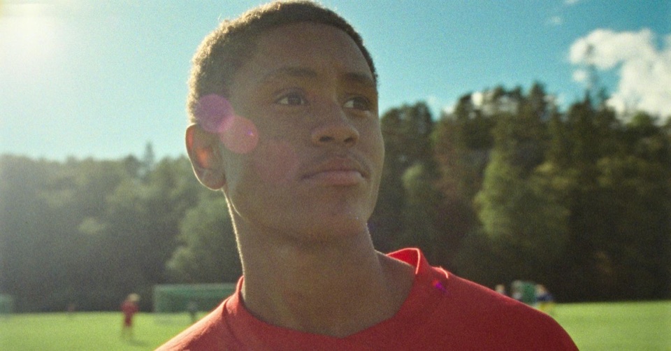 Ung gutt i rød drakt på en fotballbane i sol.